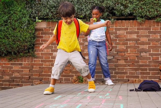 Multiethnic kids playing hopscotch on school playground while eating apples