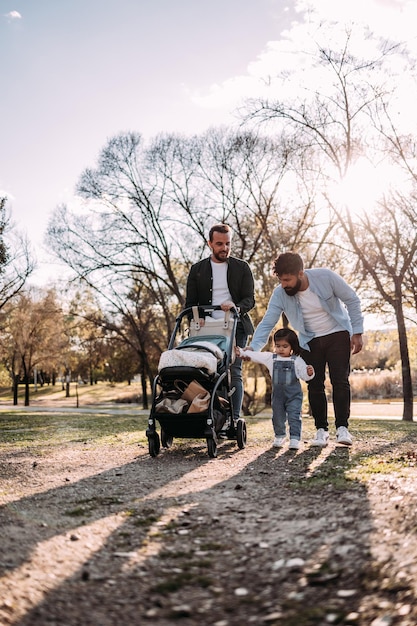 Multiethnic male gay couple walking with their little daughter in the park Modern family concept Vertical