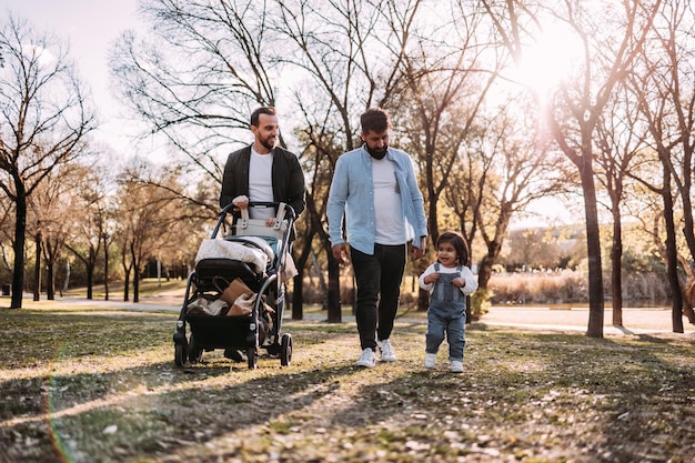 Multiethnic male gay couple walking with their little daughter in the park Modern family concept