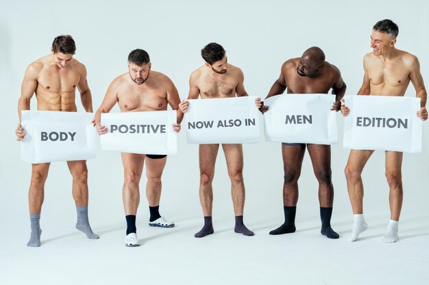 사진 남성 에디션을 위해 포즈를 취한 다민족 남성들은 현수막에 메시지를 표시하는 긍정적인 미인 세트입니다. 나이가 다른 벗은 남자와 복서 속옷을 입은 몸