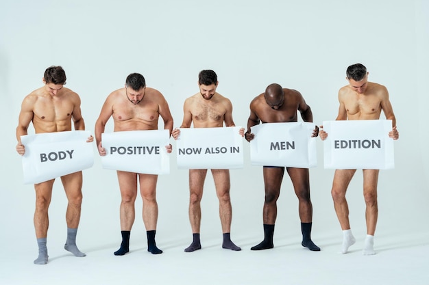 Multiethnic men posing for a male edition body positive beauty set showing messages on banners. Shirtless guys with different age, and body wearing boxers underwear