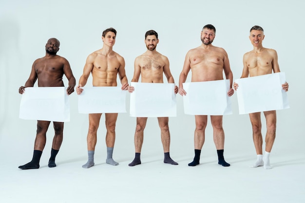 Photo multiethnic men posing for a male edition body positive beauty set showing messages on banners. shirtless guys with different age, and body wearing boxers underwear