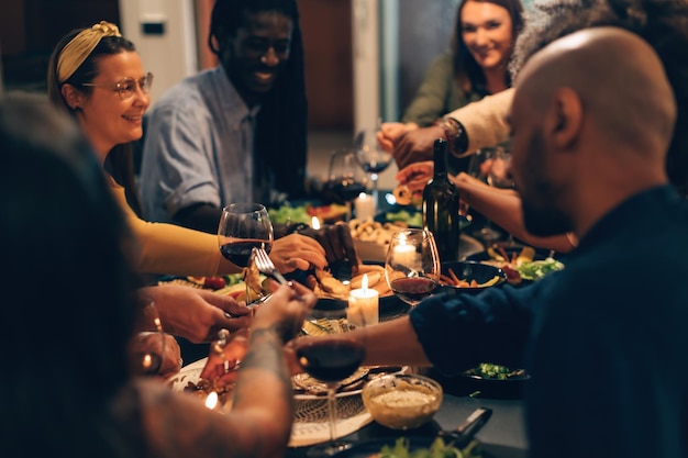 写真 家やレストランで楽しい夜に一緒に座っている多民族の人々が、菜食主義の食べ物を食べ、友情と家族生活を祝うワインを飲む