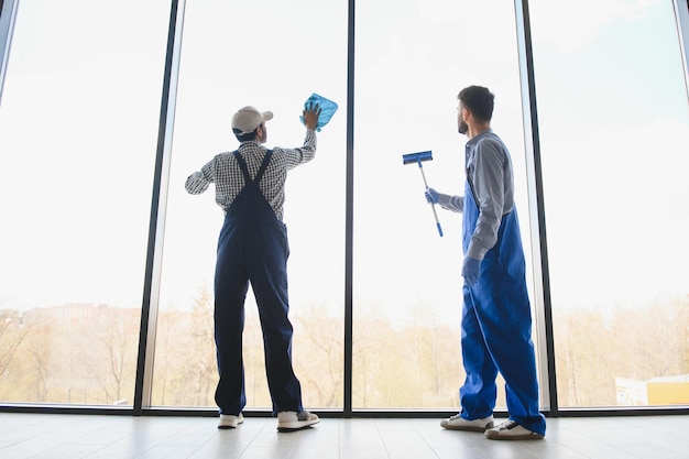 Multiethnic professional cleaners in uniform washing large windows in office