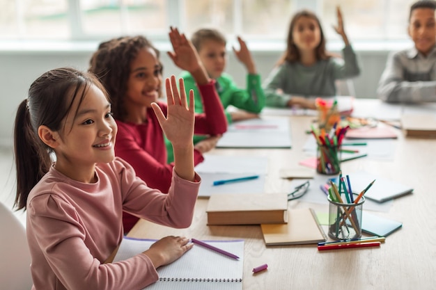 教室での授業中に腕を上げることを学ぶ多民族の学校の子供たち