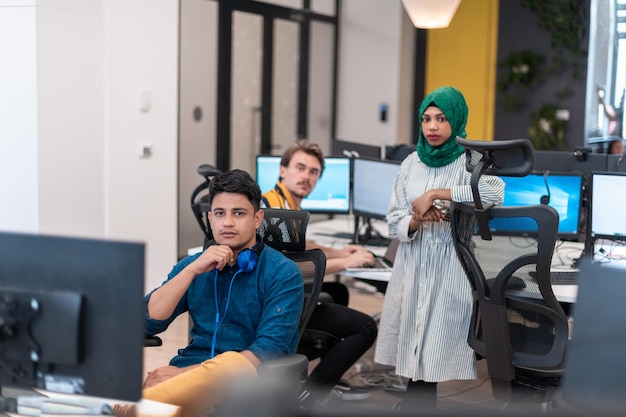多民族のスタートアップビジネスチームのアラビア人女性が、ラップトップとデスクトップコンピューターで作業している、現代のオープンプランのオフィスインテリアブレーンストーミングでの会議でヒジャーブを身に着けています。セレクティブフォーカス。高品質の写真