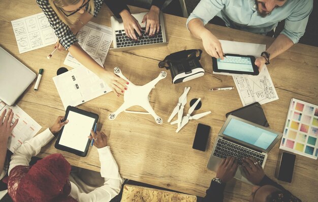 multiethnic startup business team discussing new business plan,working on laptop and tablet computer while learning about drone technology for future business ventures top view