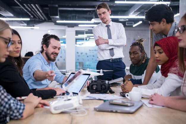 다민족 스타트업 비즈니스 팀은 새로운 비즈니스 계획에 대해 논의하고, 노트북과 태블릿 컴퓨터에서 작업하면서 새로운 비즈니스 발전을 위한 드론 기술에 대해 학습합니다.