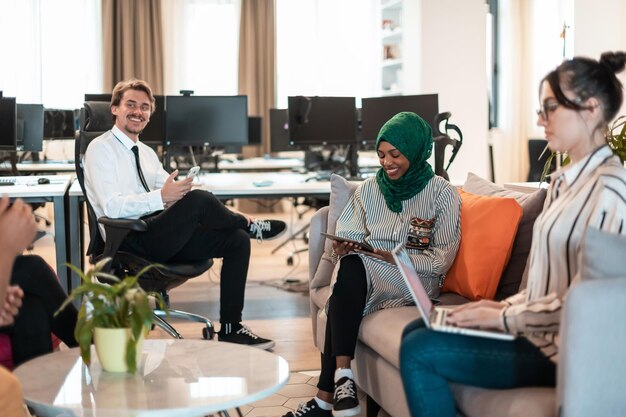 Multiethnic startup business team having brainstorming in\
relaxation area of modern office interior working on laptop and\
tablet computer. high-quality photo