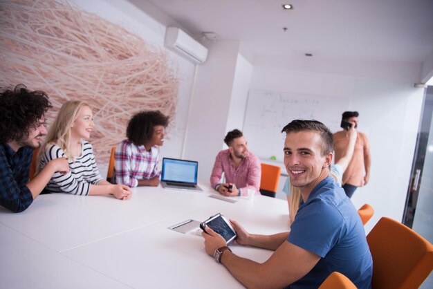 Мультиэтническая стартап-команда на встрече в современном светлом офисе проводит мозговой штурм, работает на ноутбуке и планшетном компьютере