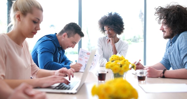 Foto team aziendale multietnico di avvio in riunione in un moderno e luminoso ufficio di brainstorming, lavorando su laptop e tablet