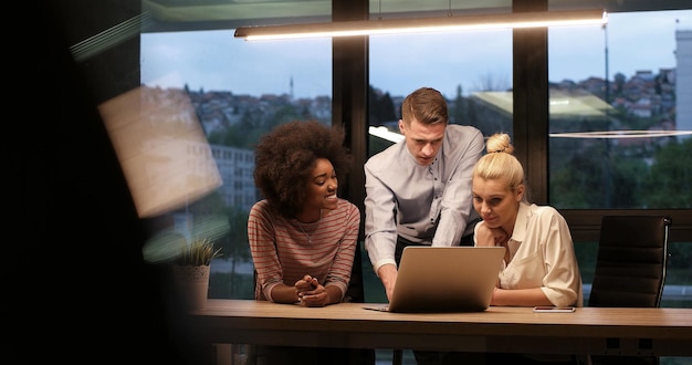 Foto team aziendale multietnico di avvio in riunione nel moderno brainstorming interno dell'ufficio notturno, lavorando su laptop