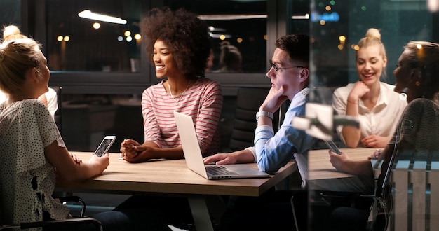 Фото Мультиэтническая стартап-команда на встрече в современном ночном офисе проводит мозговой штурм, работает на ноутбуке