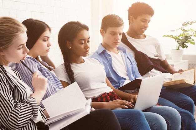 Multiethnic students preparing for exams with laptop and books