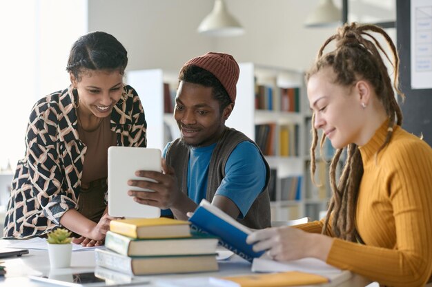 Multiethnic students watching video on digital tablet while doing homework together sitting in the library