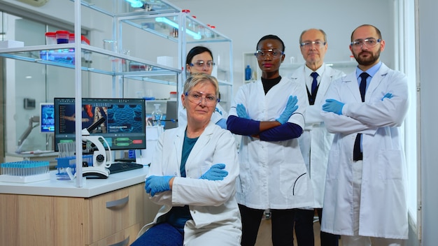 Multiethnic team of experienced scientists looking at camera in modern equipped lab. Group of doctors examining virus evolution with high tech and chemistry tools for scientific research, vaccine deve