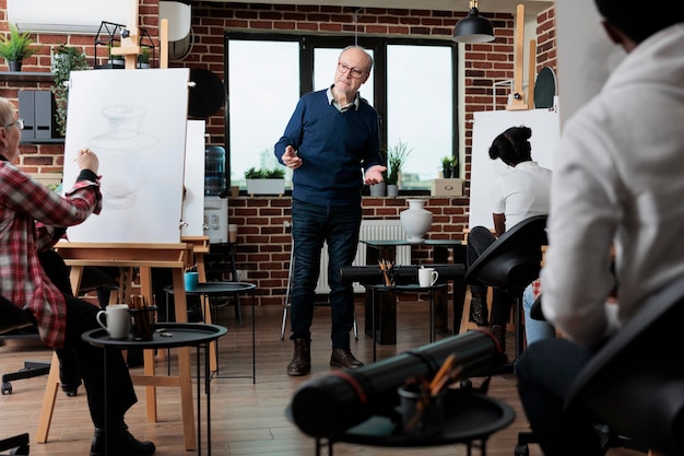 Photo multiethnic team sketching vase model on white canvas during creativity class learning how ro draw for personal growth. man teacher explaining drawing technique to students. creative activity concept