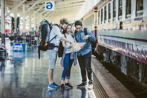 I viaggiatori multietnici stanno guardando la mappa alla stazione ferroviaria