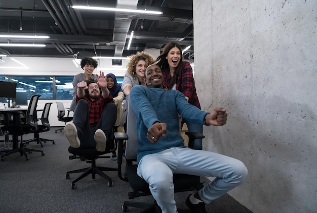 Фото Мультиэтнический стартап бизнес-команда разработчиков программного обеспечения, весело проводящая время в гонках на офисных стульях, возбужденные разнообразные сотрудники, смеющиеся, наслаждающиеся забавной деятельностью на рабочем перерыве, творческие дружелюбные работники p