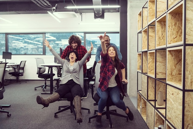 Photo multiethnics startup business team of software developers having fun while racing on office chairs,excited diverse employees laughing enjoying funny activity at work break, creative friendly workers p