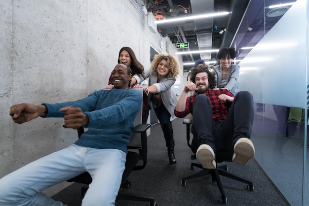 многонациональная стартап-бизнес-команда разработчиков программного обеспечения, развлекающаяся во время гонок на офисных стульях, возбужденные смехом сотрудников, веселые занятия на перерывах в работе, дружелюбные творческие работники.