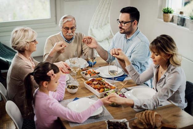 Multigeneration family holding hands while saying grace before a meal at dining table