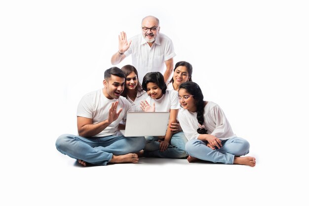 Multigenerational Indian asian family of six online shopping using laptop and electronic card while sitting against white background