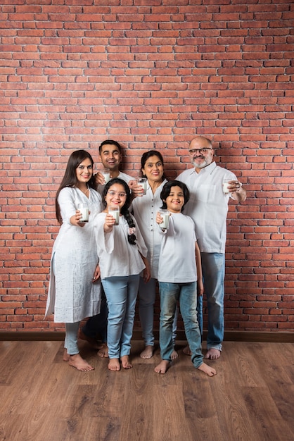 Multigenerationele Indiase Aziatische familie die glazen vol melk toont of vasthoudt tegen bakstenen muur