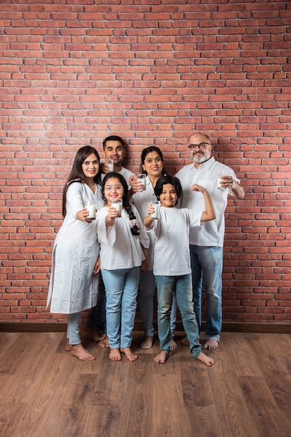 Multigenerationele Indiase Aziatische familie die glazen vol melk toont of vasthoudt tegen bakstenen muur