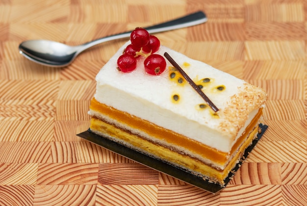 многослойный торт с воздушным кремом и красной смородиной на деревянном фоне, маленькая ложка