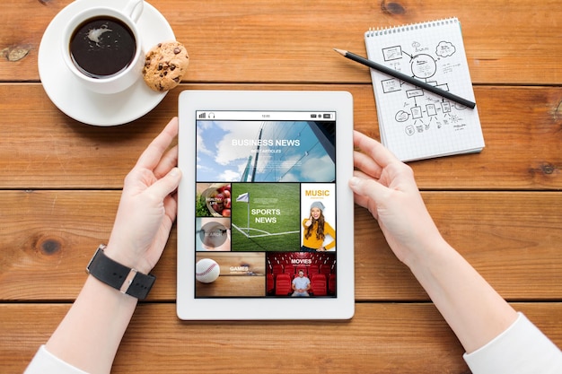 マルチメディア、ビジネス、教育、技術、人々のコンセプト – タブレットPCのコンピュータ画面にインターネットニュースアプリケーション、木製のテーブルにコーヒーを持つ女性の接写