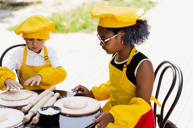 Multinationaal bedrijf van kinderen kookt in gele uniformen deeg koken voor bakkerij Afrikaanse tiener en zwart meisje veel plezier met blanke kindjongen en koken voedsel