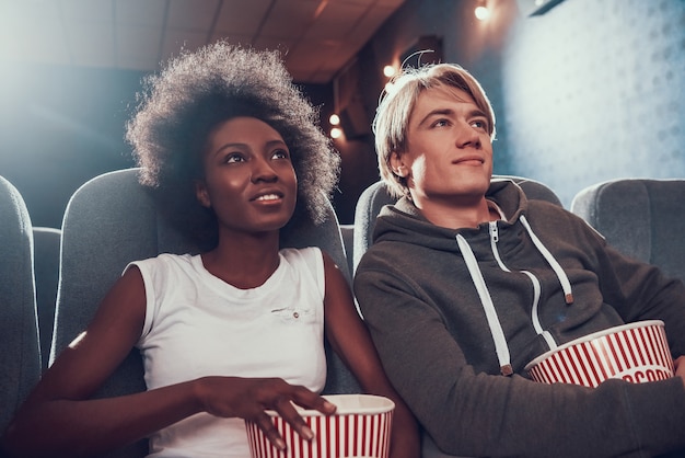 Многонациональная пара с попкорном сидит в кинотеатре
