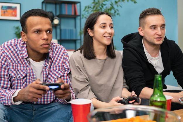 Multinational friends sitting at home on couch and playing video games on console cheerful woman hav