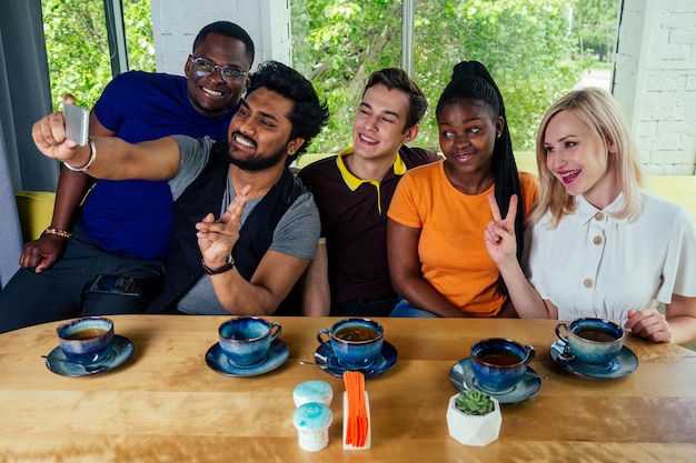 Multinational group of happy friends enjoy and drinking tea and taking photos selfie on photocamera in cafe