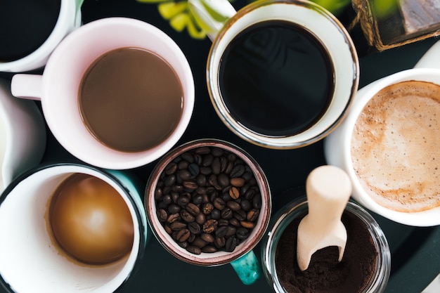 Несколько чашек кофе, молока, зерен и молотого кофе в банке на черном фоне. Фото высокого качества