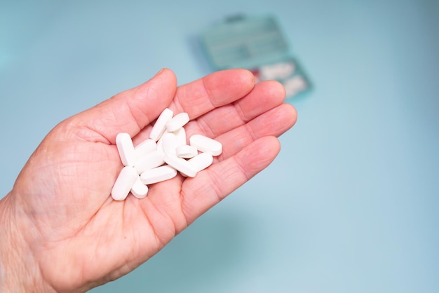 Multiple colours pills in senior hand on blue background. Taking Your Medication. Medicine concept.