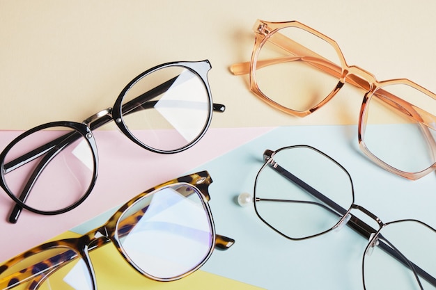 Multiple eyeglasses on a multicolored background of pastel colors, geometric background, pink yellow and light blue colors, trendy eyeglass frames copy space