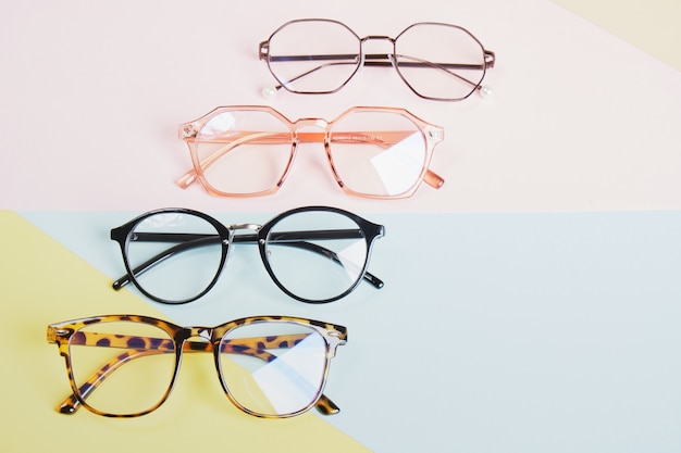 Photo multiple eyeglasses on a multicolored background of pastel colors, geometric background, pink yellow and light blue colors, trendy eyeglass frames copy space