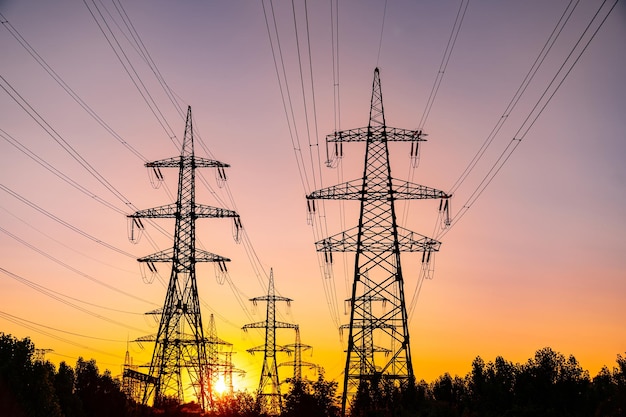 Multiple highvoltage towers silhouettes at sundown Power lines at beautiful pink sunset light Electricity power pylons in the last rays of setting sun