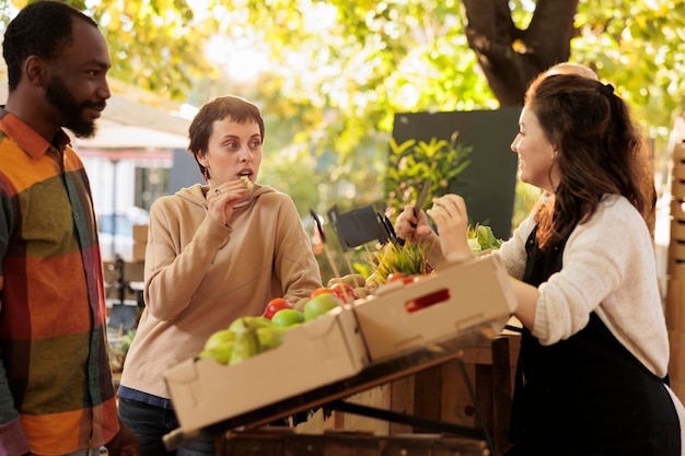 Foto multiraciaal stel dat bio-biologische producten proeft op de boerenmarkt en lokaal geteelde groenten en fruit verkoopt op de boerenmarkt. jonge familie die natuurlijke eco-producten proeft, voedselmonsters.