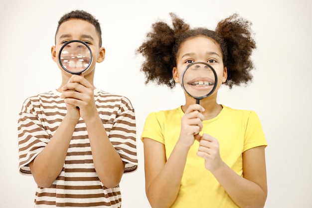 Photo multiracial boy and girl holding two magnifying glasses near their mouth