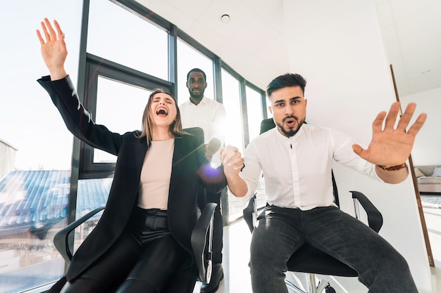 Multiracial business people staged crazy office games on chairs