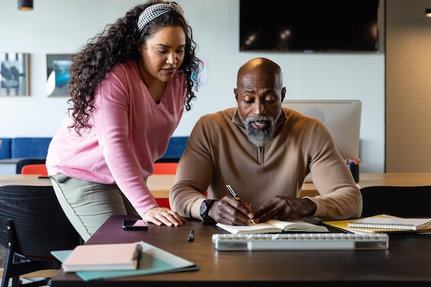 Multiracial businessman and businesswoman discussing over diary in creative office