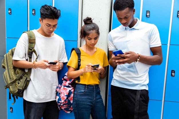 Photo multiracial classmates using mobile phone with disinterest on each other in high school corridor