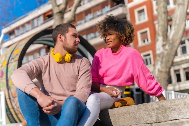 Multiracial couple on the city streets lifestyle sitting looking at each other and smiling