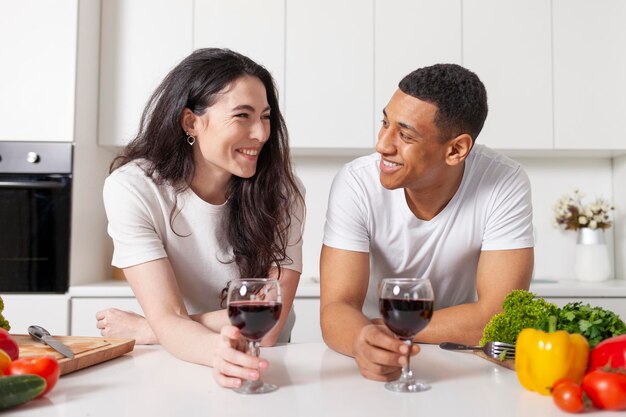 Photo multiracial couple drinking wine in the kitchen and talking american guy and european girl