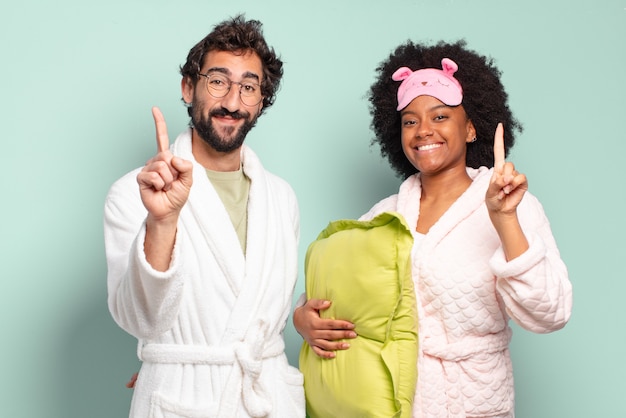 Multiracial couple of friends smiling and looking friendly, showing number one or first with hand forward, counting down.