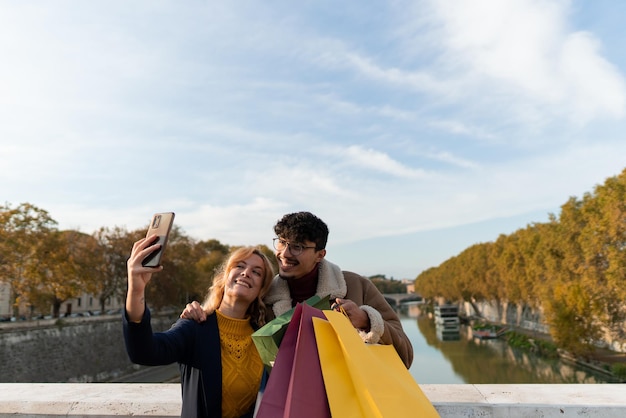 Multiracial couple of friends taking a very happy selfie holding shopping bags
