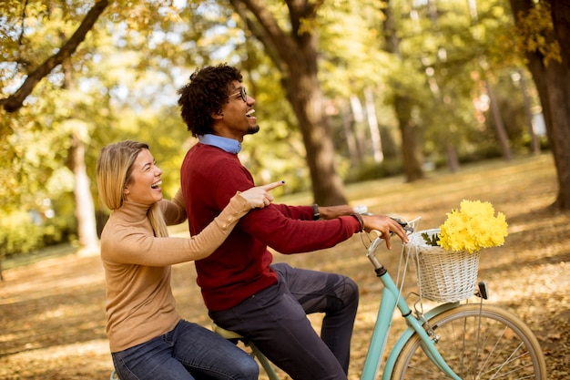 Многорасовая пара катается на велосипеде в осеннем парке